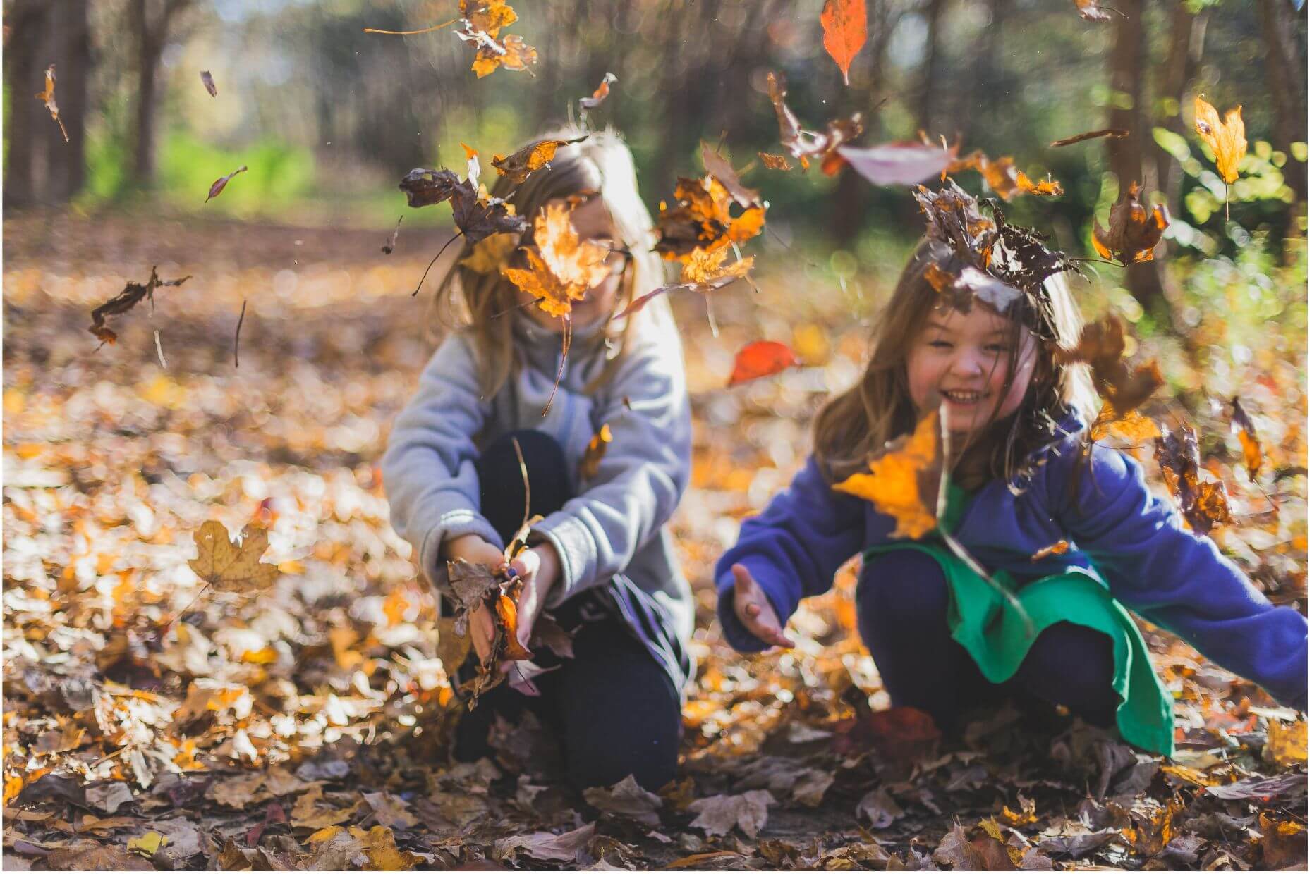 Zwei Kinder spielen im Sonnenschein mit Herbstlaub.