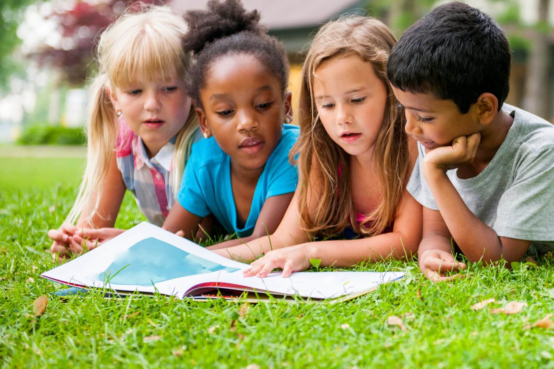 Viel Kinder liegen im Gras und lesen gemeinsam in einem Buch.