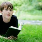 Ein Jugendlicher liegt im Gras und schaut von einem Buch auf.