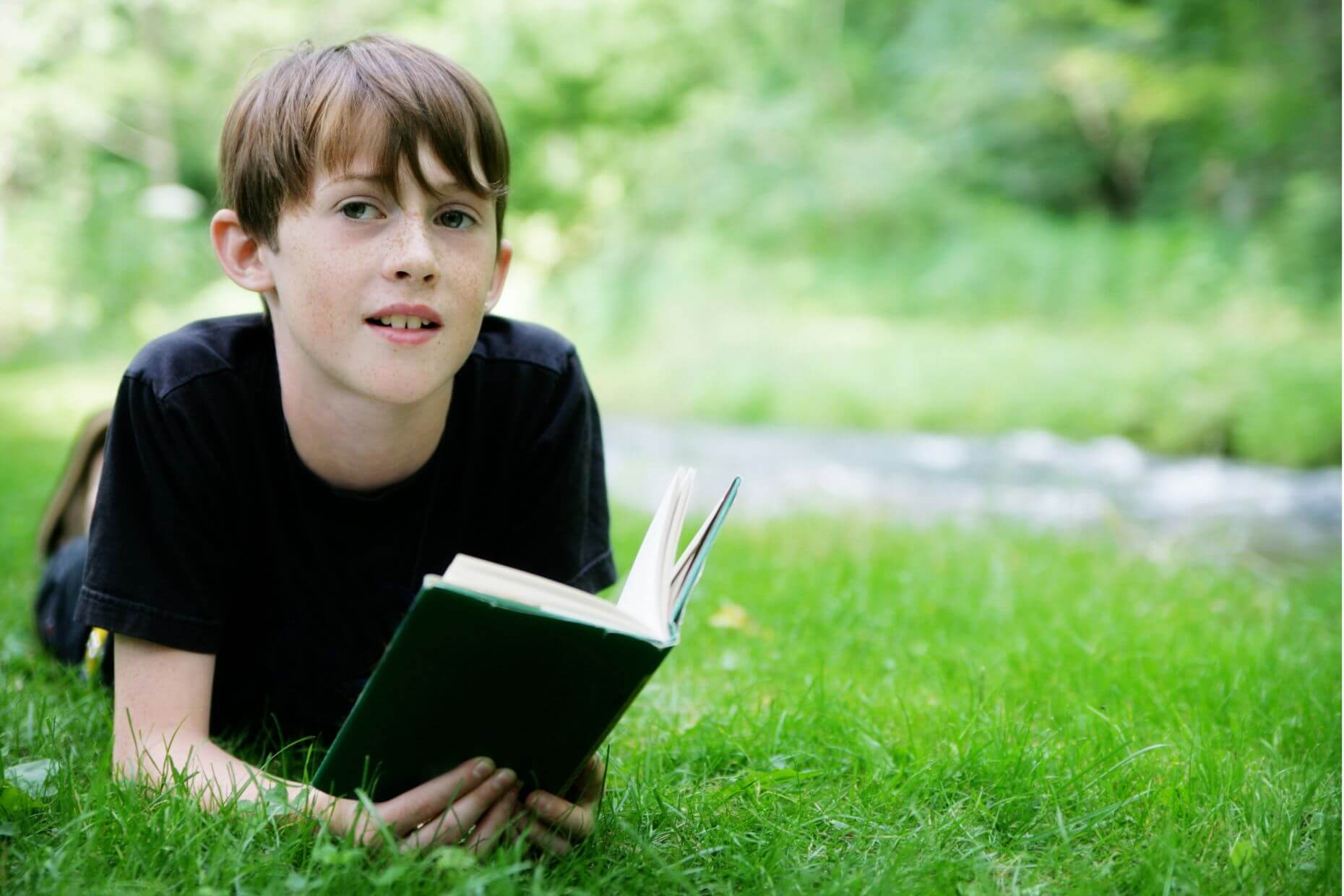Ein Jugendlicher liegt im Gras und schaut von einem Buch auf.