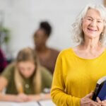 Eine lächelnde ältere Frau hält Bücher im Arm.