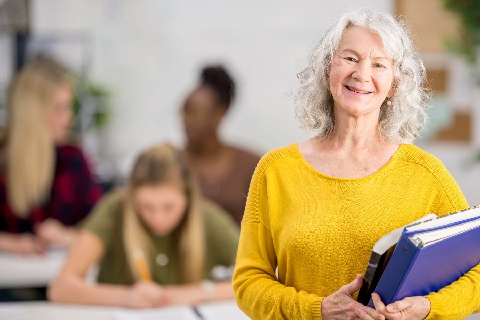 Eine lächelnde ältere Frau hält Bücher im Arm.