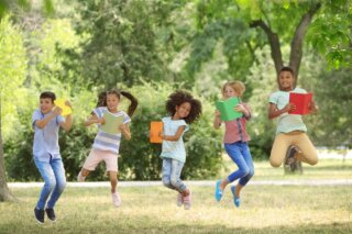 Kinderbuch Fünf Kinder hüpfen in einem Park in die Luft, jedes hält ein Buch in den Händen.