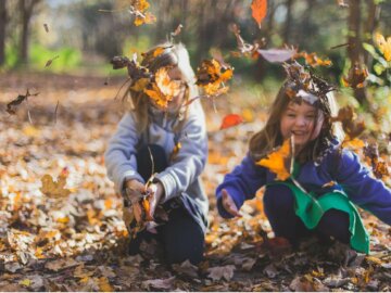 Waldkinder Zwei Kinder spielen im Sonnenschein mit Herbstlaub.