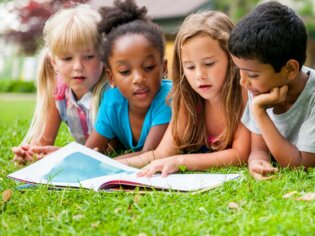 Viel Kinder liegen im Gras und lesen gemeinsam in einem Buch.