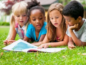 Lesen in der Natur Viel Kinder liegen im Gras und lesen gemeinsam in einem Buch.