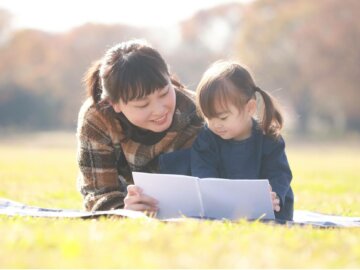 Schreibworkshop Familien Eine Frau und ein Kind lesen zusammen ein Buch in einem Park.