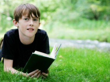 Zukunftsgeschichten Ein Jugendlicher liegt im Gras und schaut von einem Buch auf.