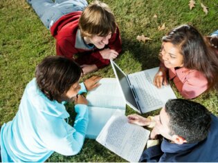 Vier Jugendliche liegen im Gras und bearbeiten gemeinsam einen Text.