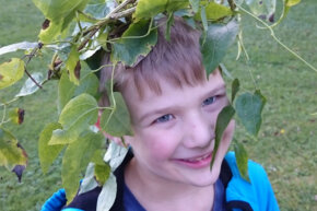 Ein lächelnder Junge trägt einen Blätterkranz auf dem Kopf.